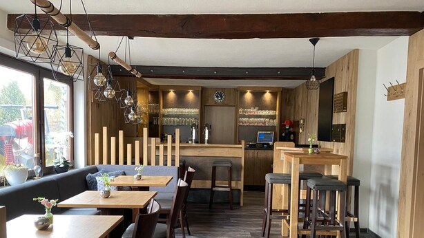 Um restaurante acolhedor com mobiliário de madeira, um bar e uma grande janela com vista para o exterior.