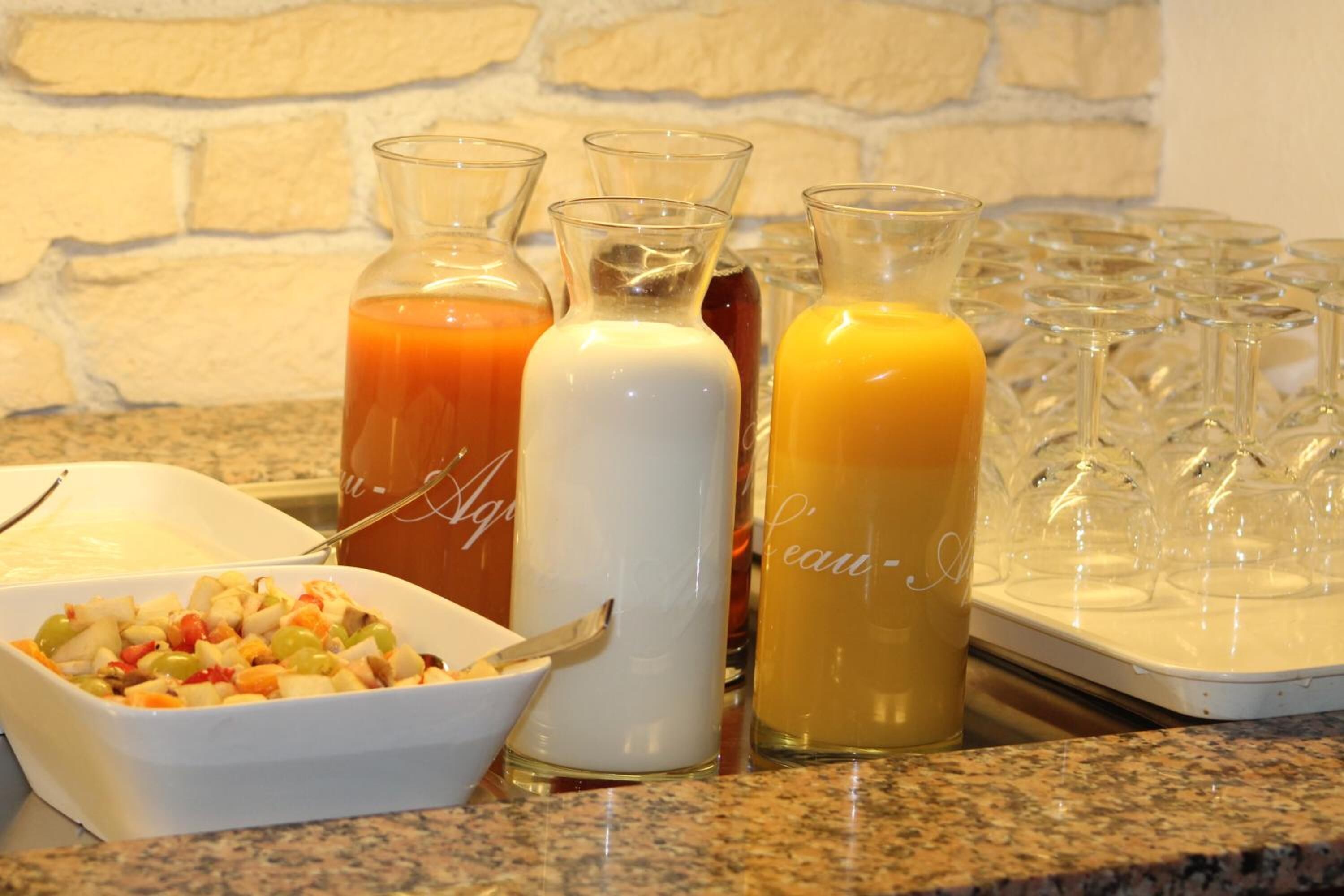 A breakfast buffet with various juices, a bowl of fruit salad, and a tray of glasses.