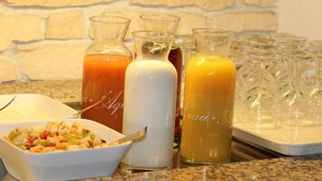 A breakfast buffet with various juices, a bowl of fruit salad, and a tray of glasses.
