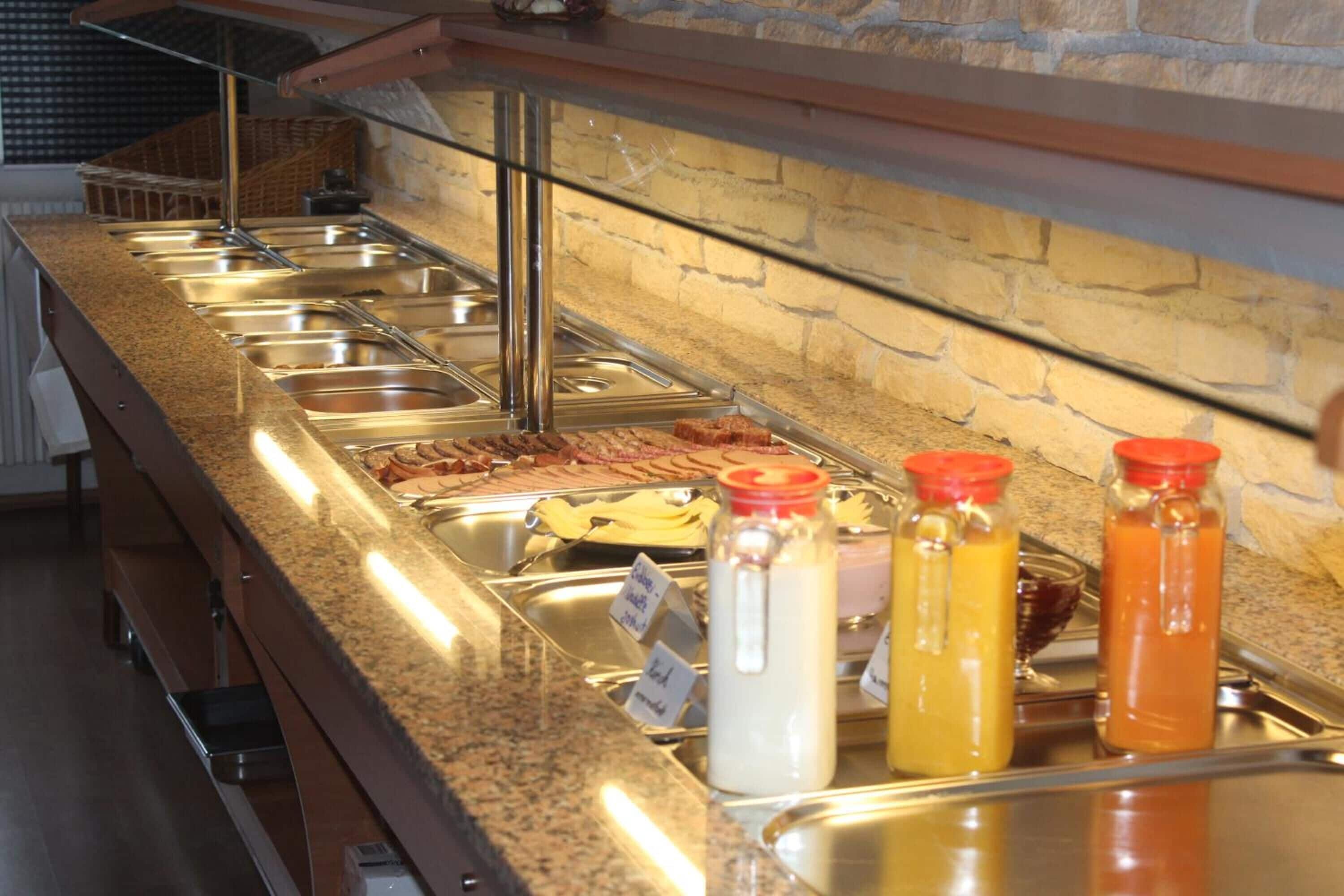 A buffet area with multiple stainless steel serving stations and a variety of condiments in glass bottles.