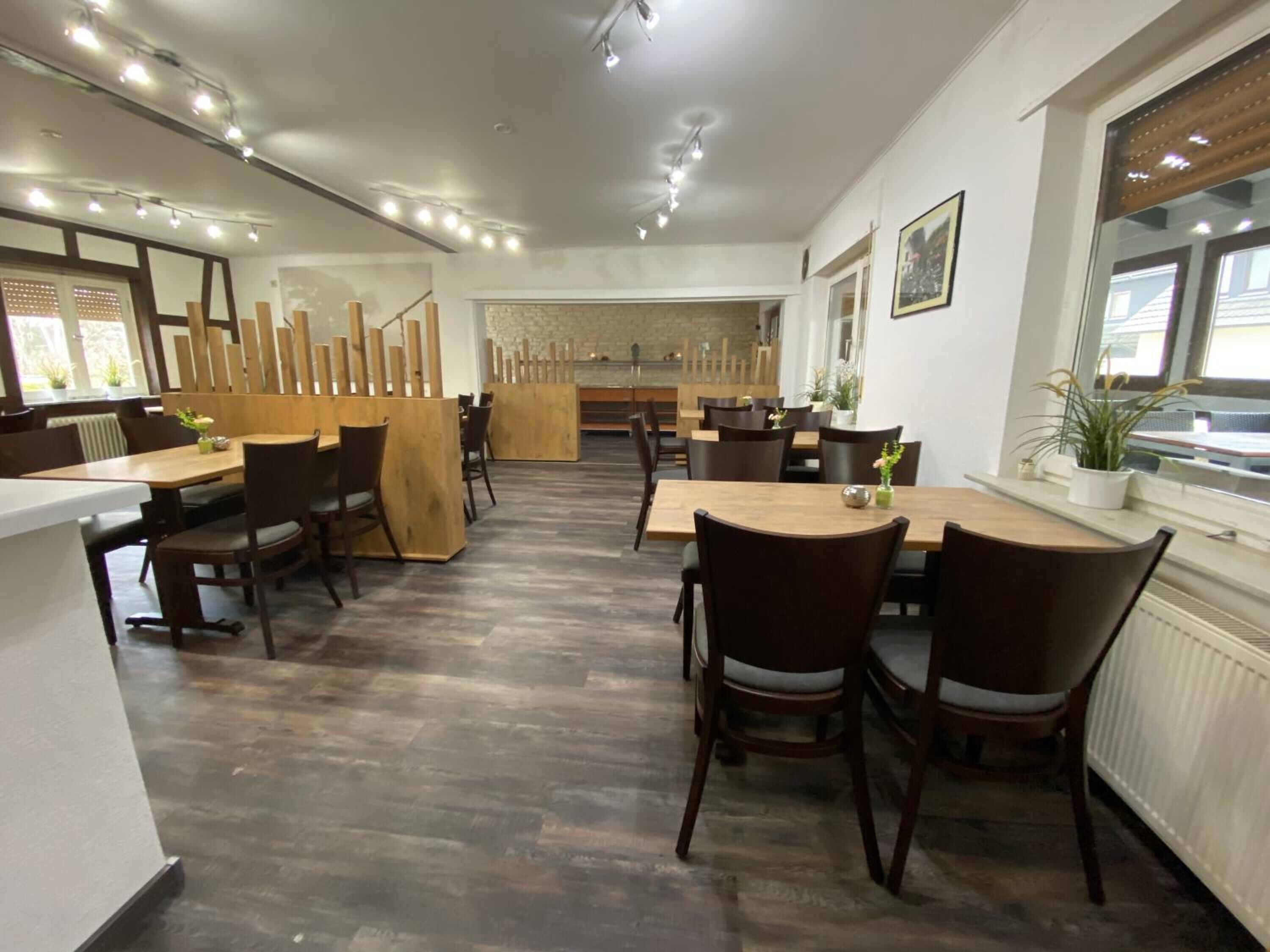 A restaurant with wooden tables and chairs, a stone wall, and a window with plants.
