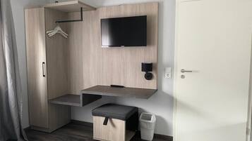 A modern room with a built-in wardrobe, a flat-screen TV mounted on the wall, a small bench, and a waste bin.