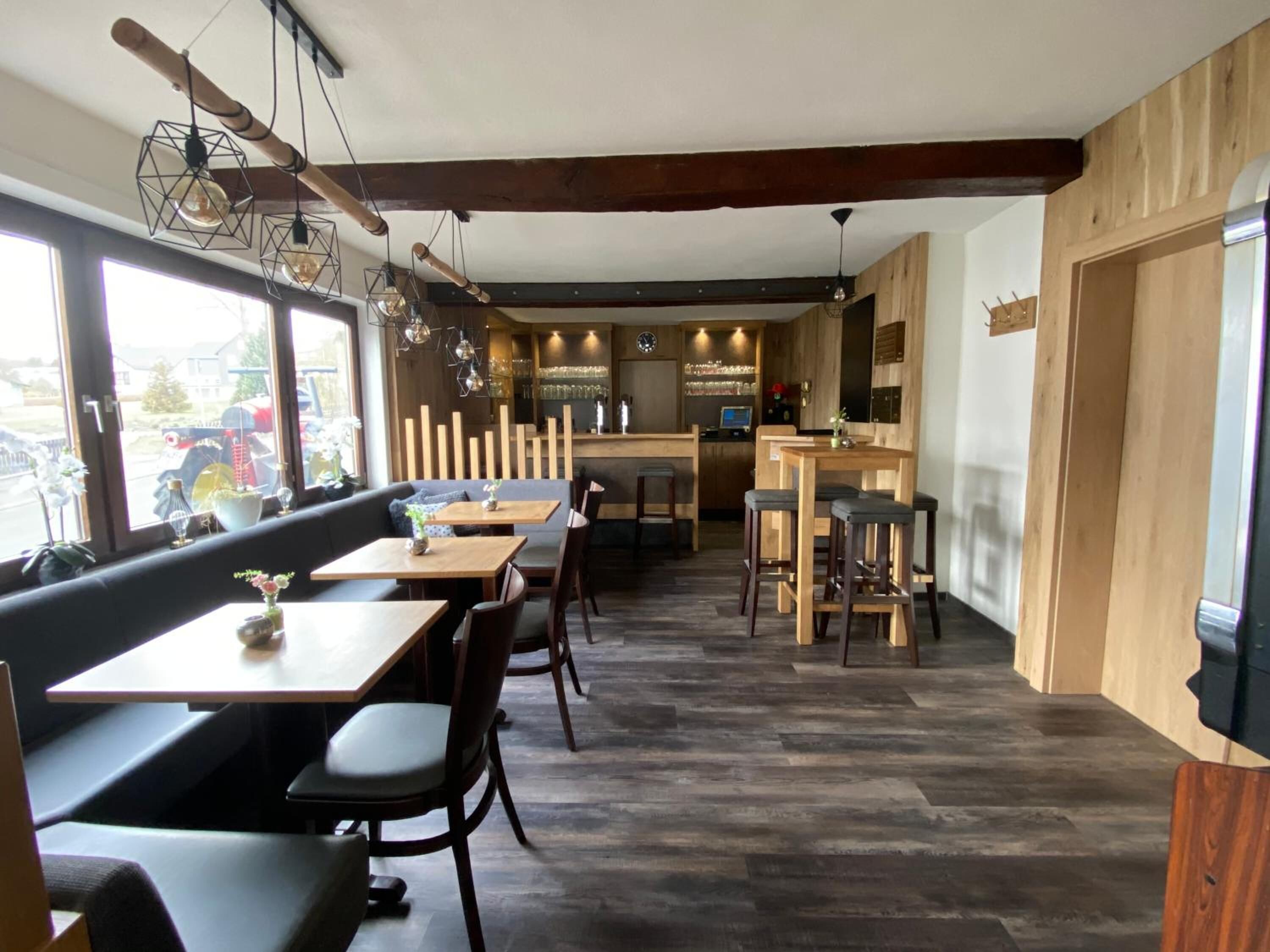 Un restaurante con mobiliario de madera, una zona de bar y ventanas amplias.