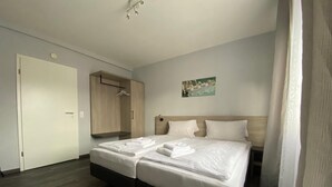 Quarto de hotel com uma cama de casal, um guarda-roupa, um quadro na parede e uma porta.