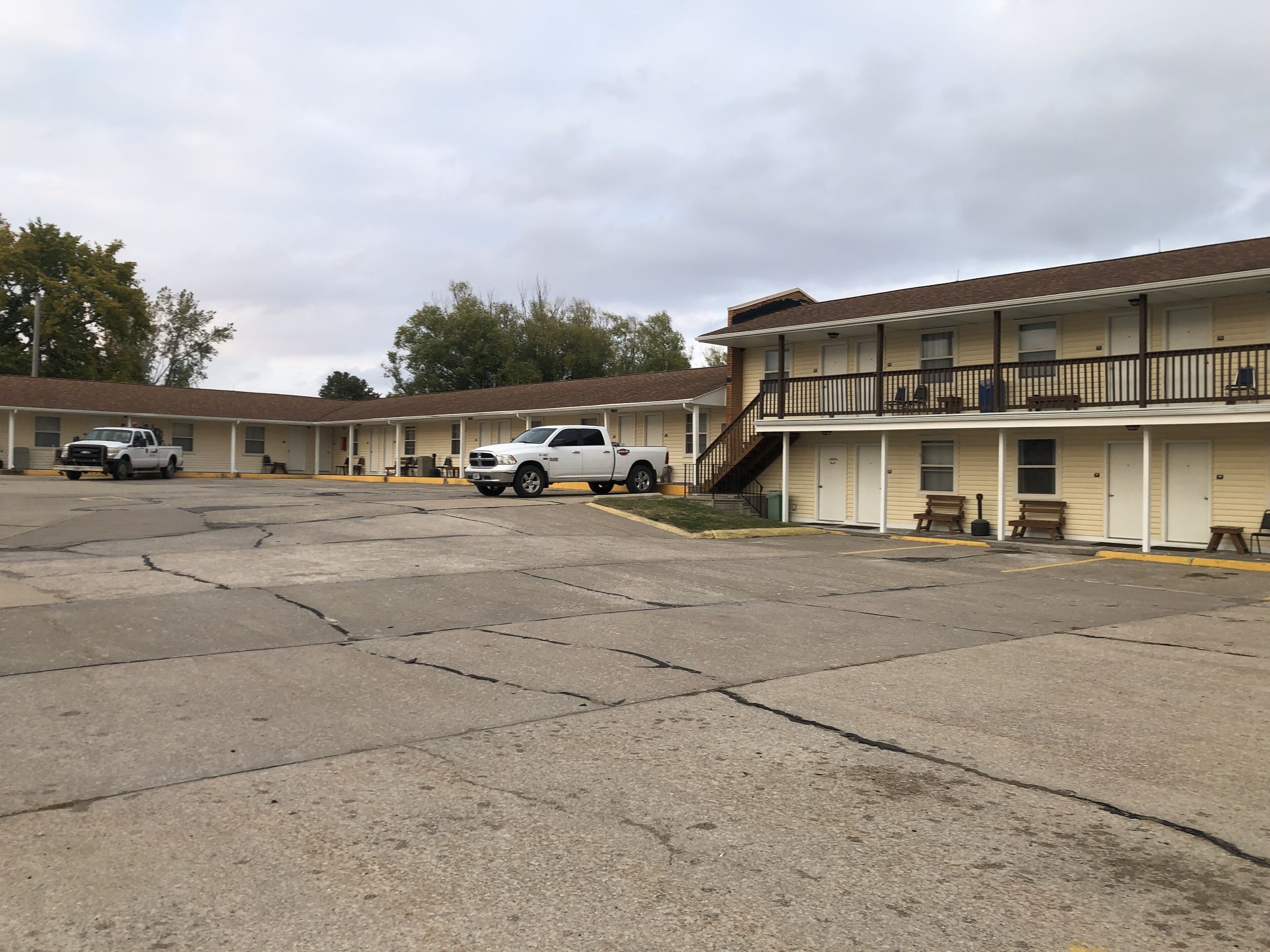 Un motel con varias habitaciones, un estacionamiento y una escalera que lleva al segundo piso.