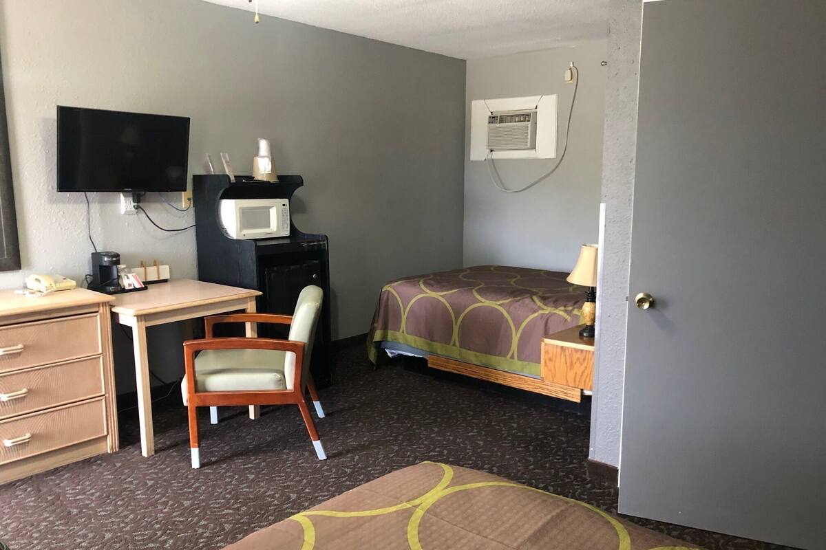 Une chambre d’hôtel équipée d’un lit, d’un bureau, d’une chaise, d’une télévision, d’un four à micro-ondes, d’une machine à café et d’une porte.