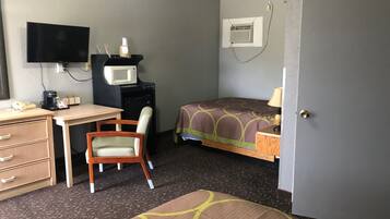 A hotel room with a bed, a desk, a chair, a television, a microwave, a coffee maker, and a door.