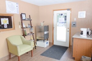 Una habitación pequeña y bien iluminada con kitchenette, una silla, un estante con varios objetos y una puerta que da al exterior.
