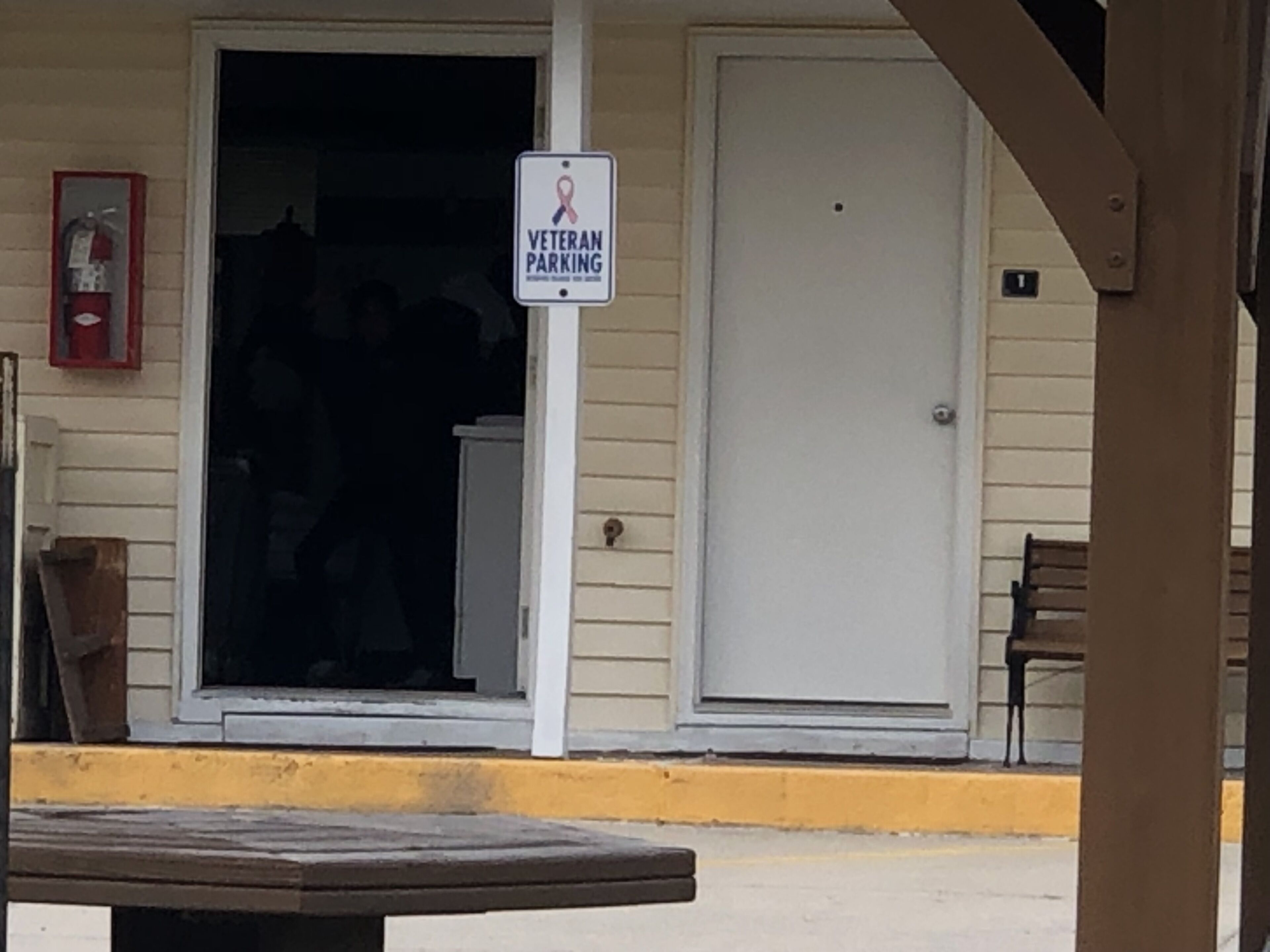 Entrada de un edificio con un cartel que dice 'Veteran Parking', una puerta y un banco afuera.