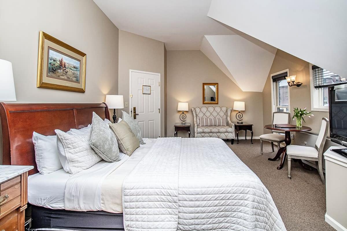 A hotel room with a large bed, a wooden headboard, a chair, a desk, a television, and a framed picture on the wall.