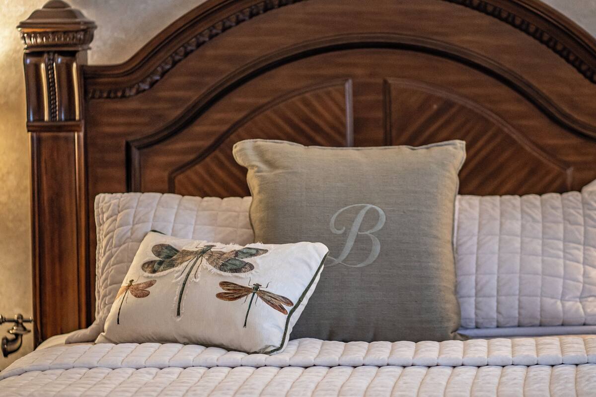 A neatly made bed with a quilted bedspread, a pillow with a monogram, and a wooden headboard.