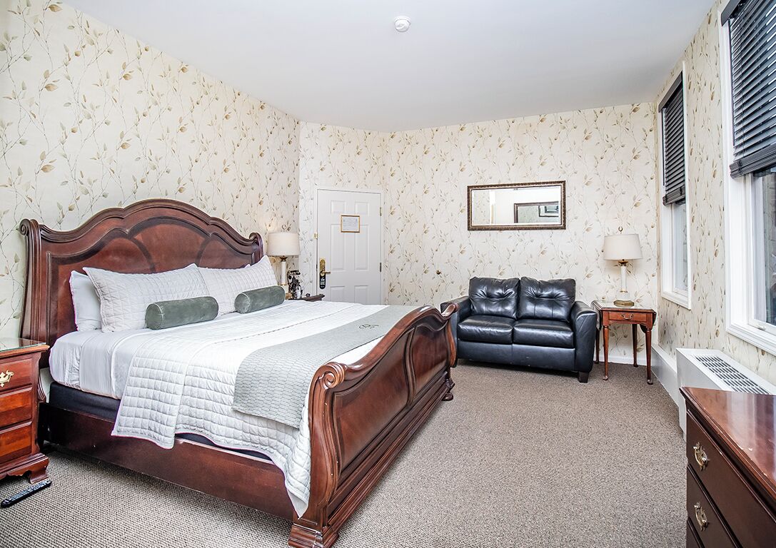 A bedroom with a large wooden bed, a black leather sofa, a small table, and a mirror on the wall.