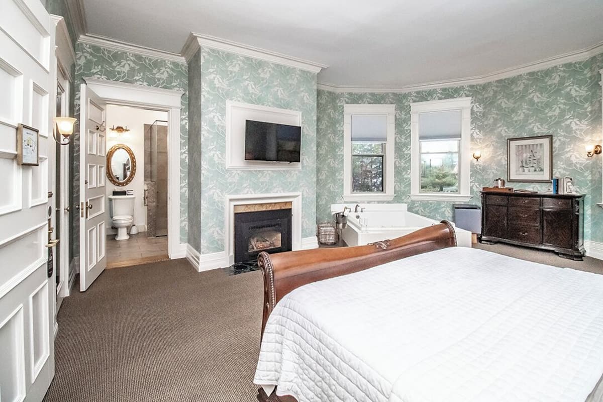 A bedroom with a large bed, a fireplace, a television, and a dresser.