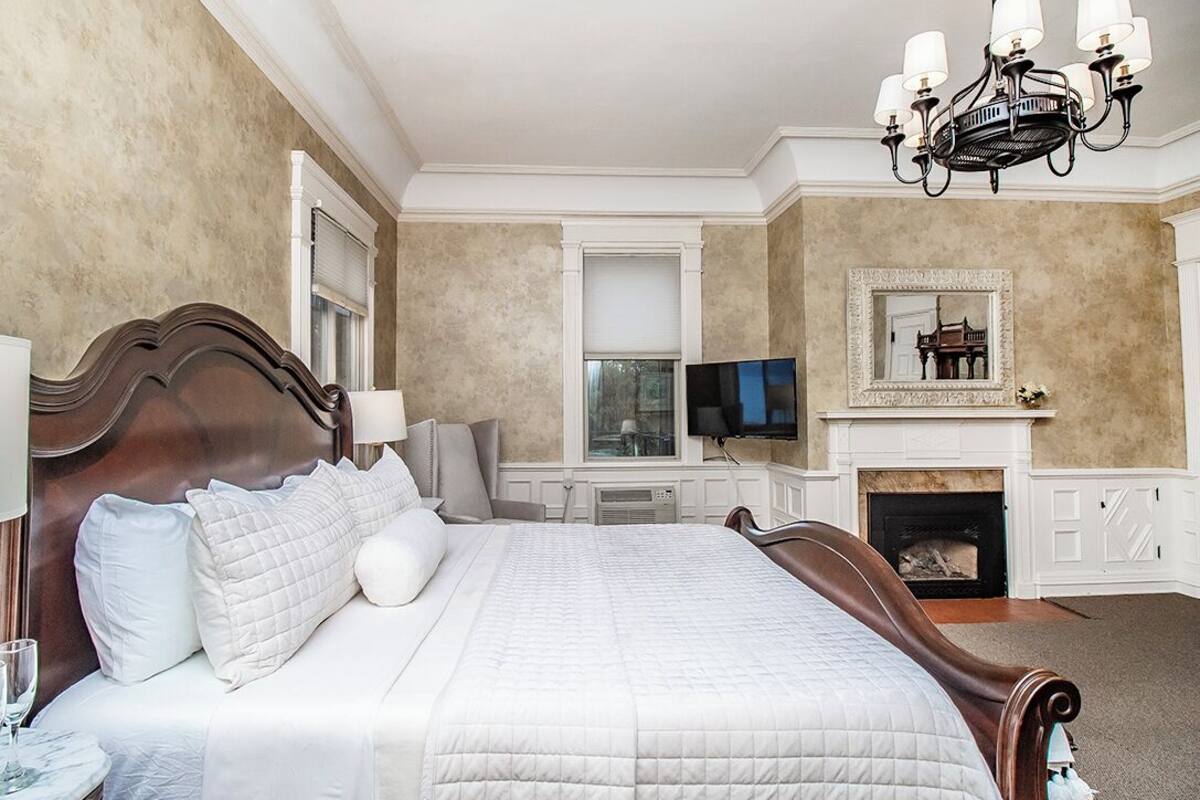A spacious bedroom with a large bed, a television, a fireplace, and a chandelier.