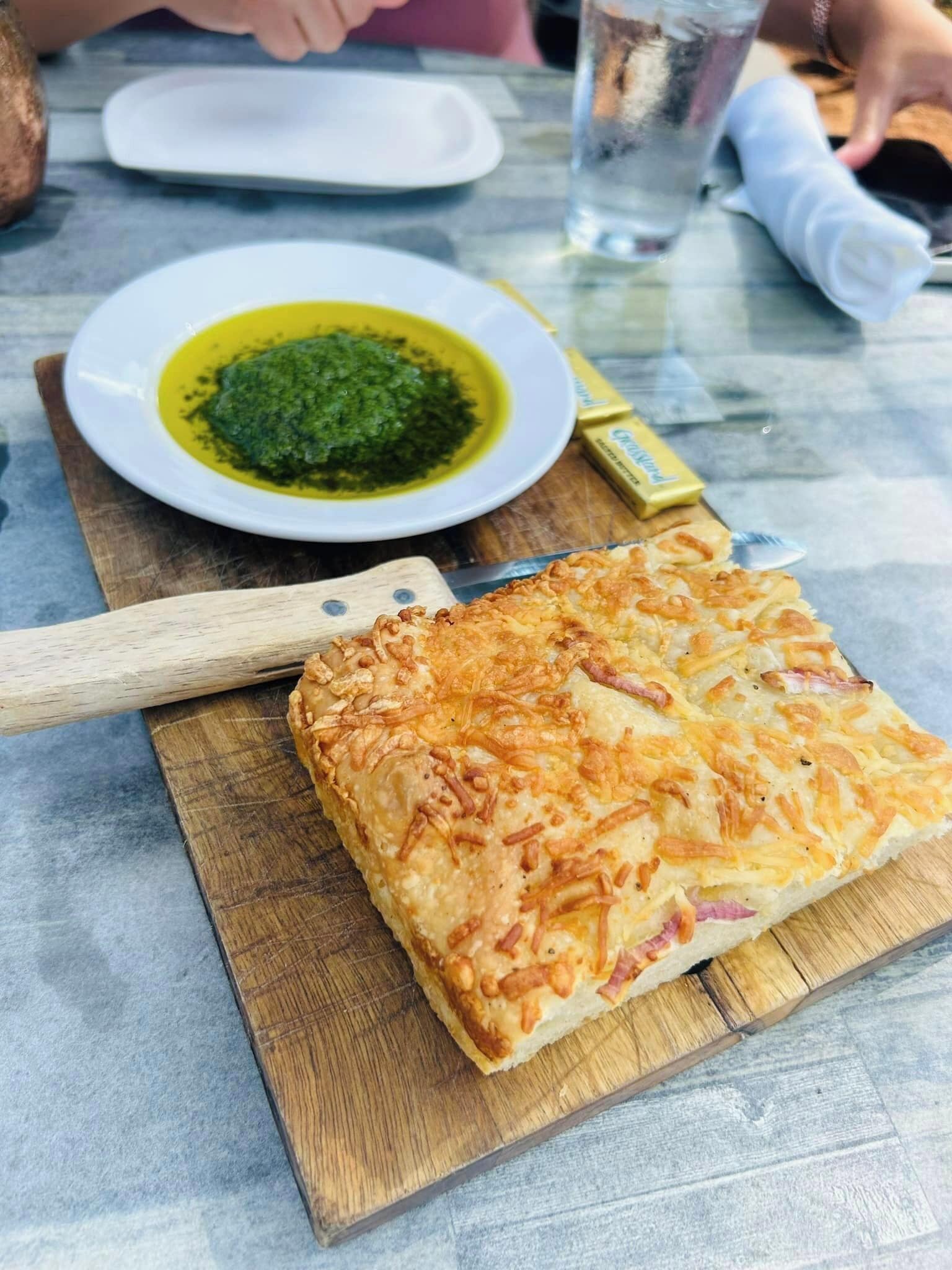 A meal with a baked dish on a wooden board, a plate with green sauce, and a small container of butter.