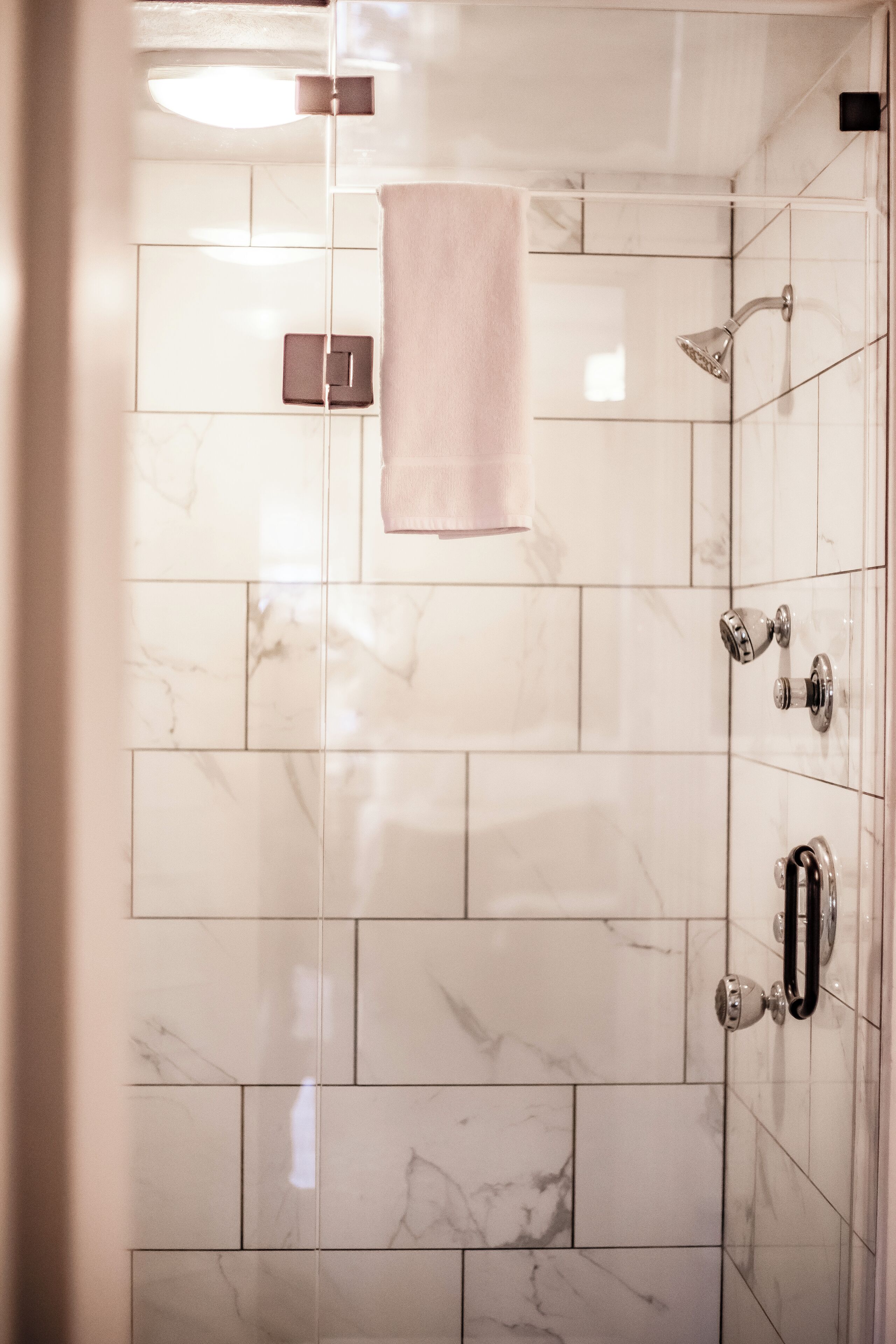 Un baño con baldosas de mármol blanco, una ducha con cabezal de ducha manual y una toalla colgada en la pared.