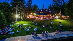 A large outdoor gathering area with a central lawn and surrounding seating, a wooden deck, and a building with multiple windows and a flag. - The Brewster Inn (Cazenovia)