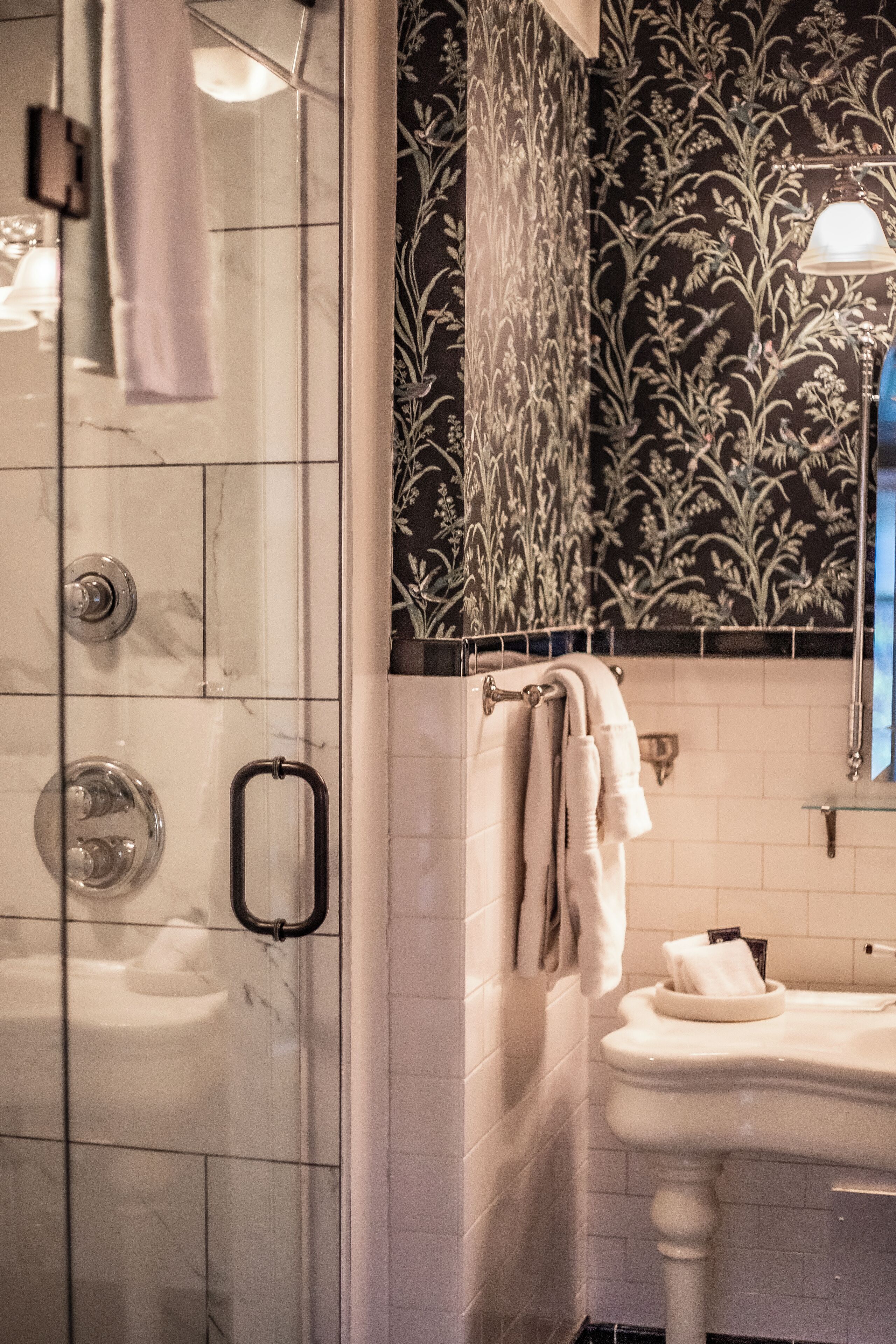 A bathroom with a glass-enclosed shower, a white sink, and a decorative wall with floral patterns.