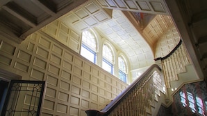 A grand staircase with ornate railings and a high ceiling with decorative panels. - The Brewster Inn (Cazenovia)