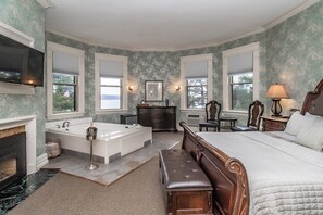 A spacious bedroom with a large bed, a sitting area, a fireplace, a bathtub, and a vanity. - The Brewster Inn (Cazenovia)