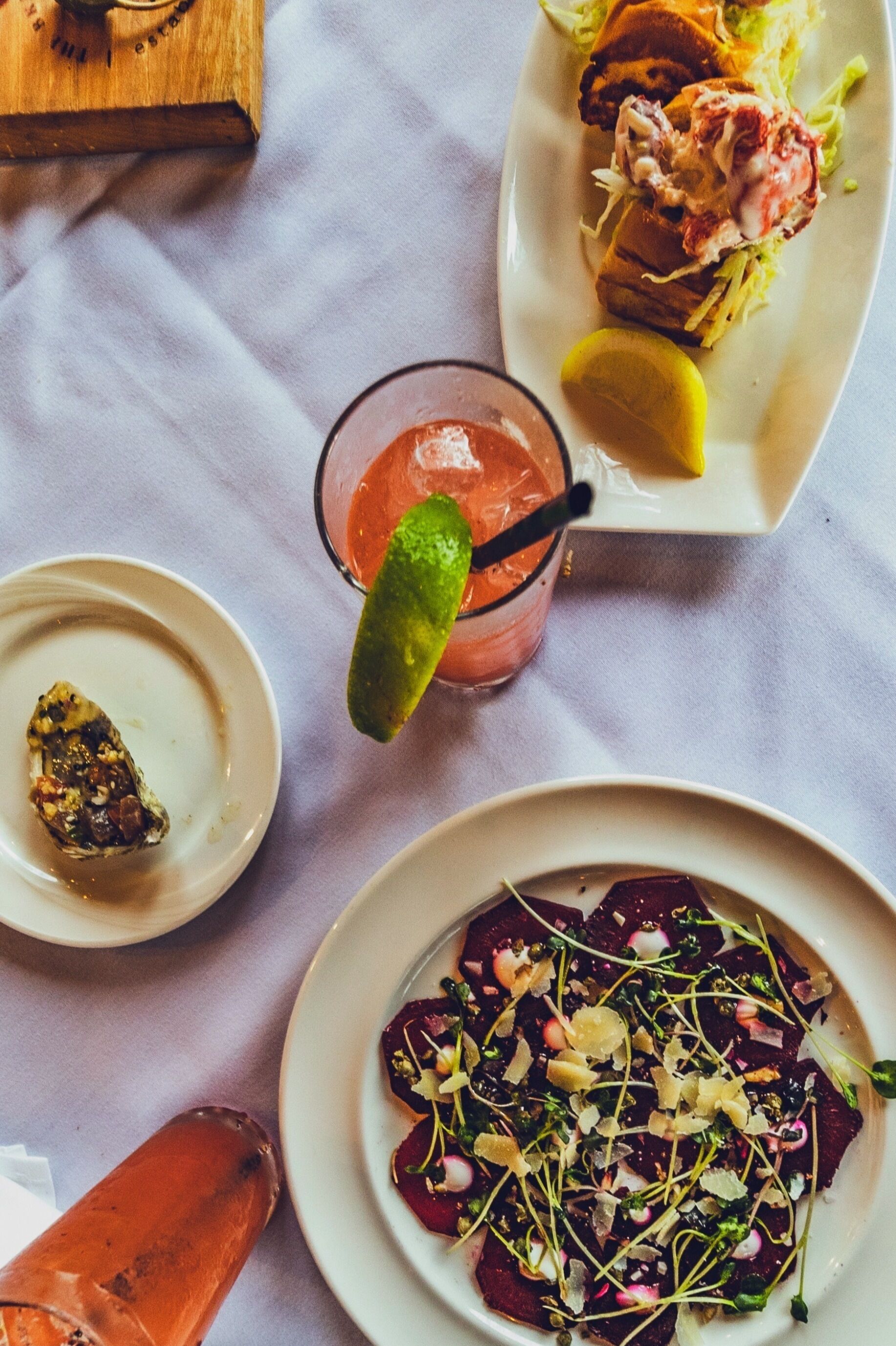 Una mesa con varios platos, una bebida adornada con lima y una botella de vino rosado.