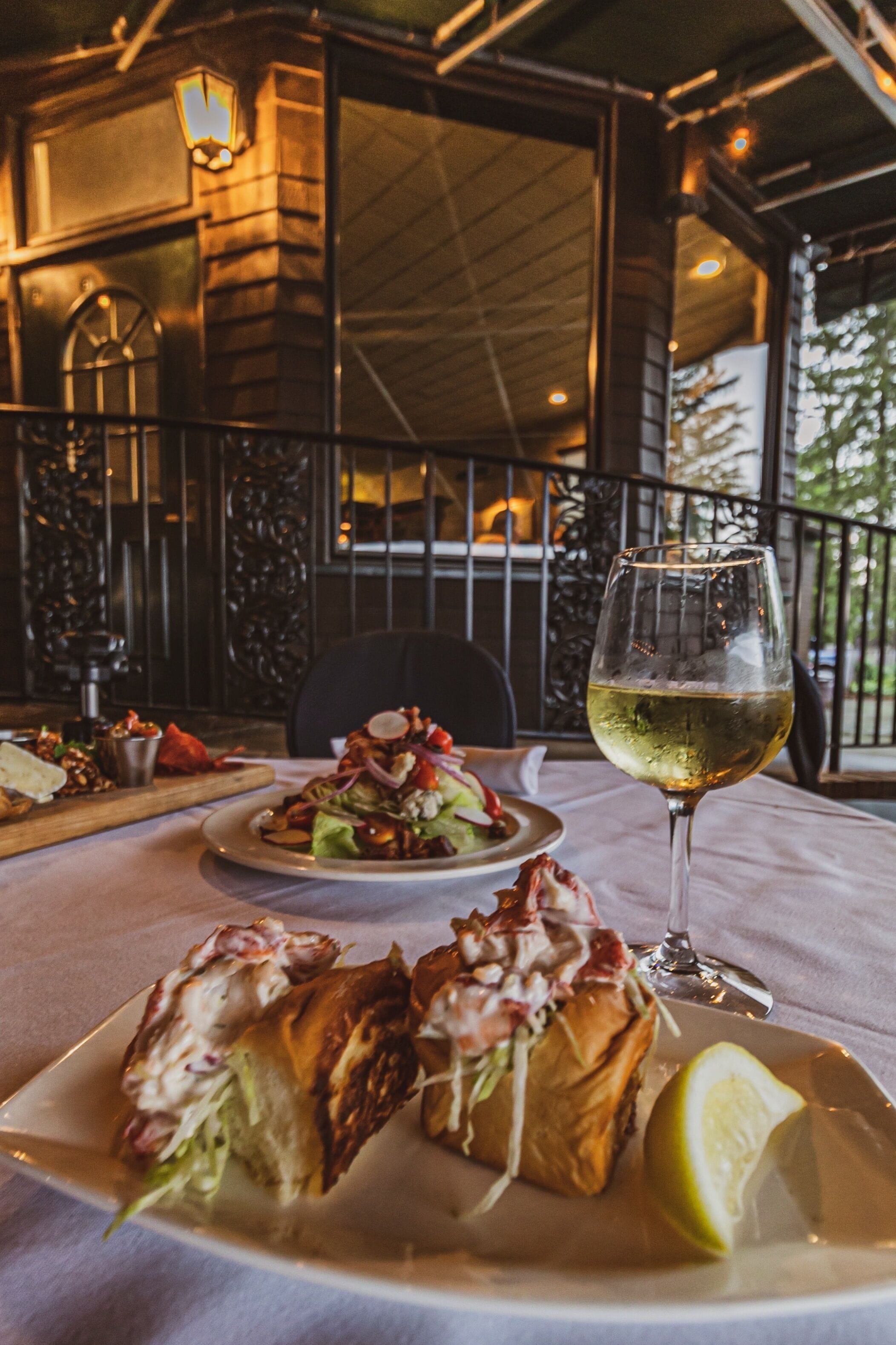 Una mesa de comedor con un plato de comida, una copa de vino blanco y un gajo de limón.