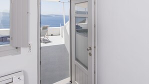 A room with a door leading to a balcony with a view of the sea. - Ambition Suites (Santorini)
