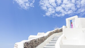 A white staircase leading to a door with a stone wall on one side. - Ambition Suites (Santorini)