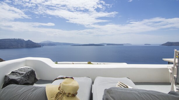 A white outdoor seating area with a view of the sea and islands. - Ambition Suites (Santorini)