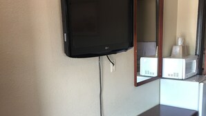 A hotel room with a wooden dresser, a flat-screen TV mounted on the wall, a microwave, and a mirror. - Best Value Inn Motel Sandusky (Marianna)