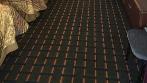 A hotel room with a checkered floor, a bed with patterned bedding, a desk, and a wall-mounted TV. - Best Value Inn Motel Sandusky (Marianna)