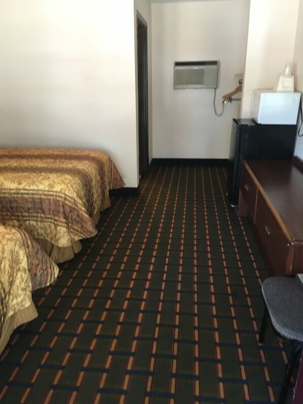 A hotel room with a checkered floor, a bed with patterned bedding, a desk, and a wall-mounted TV.