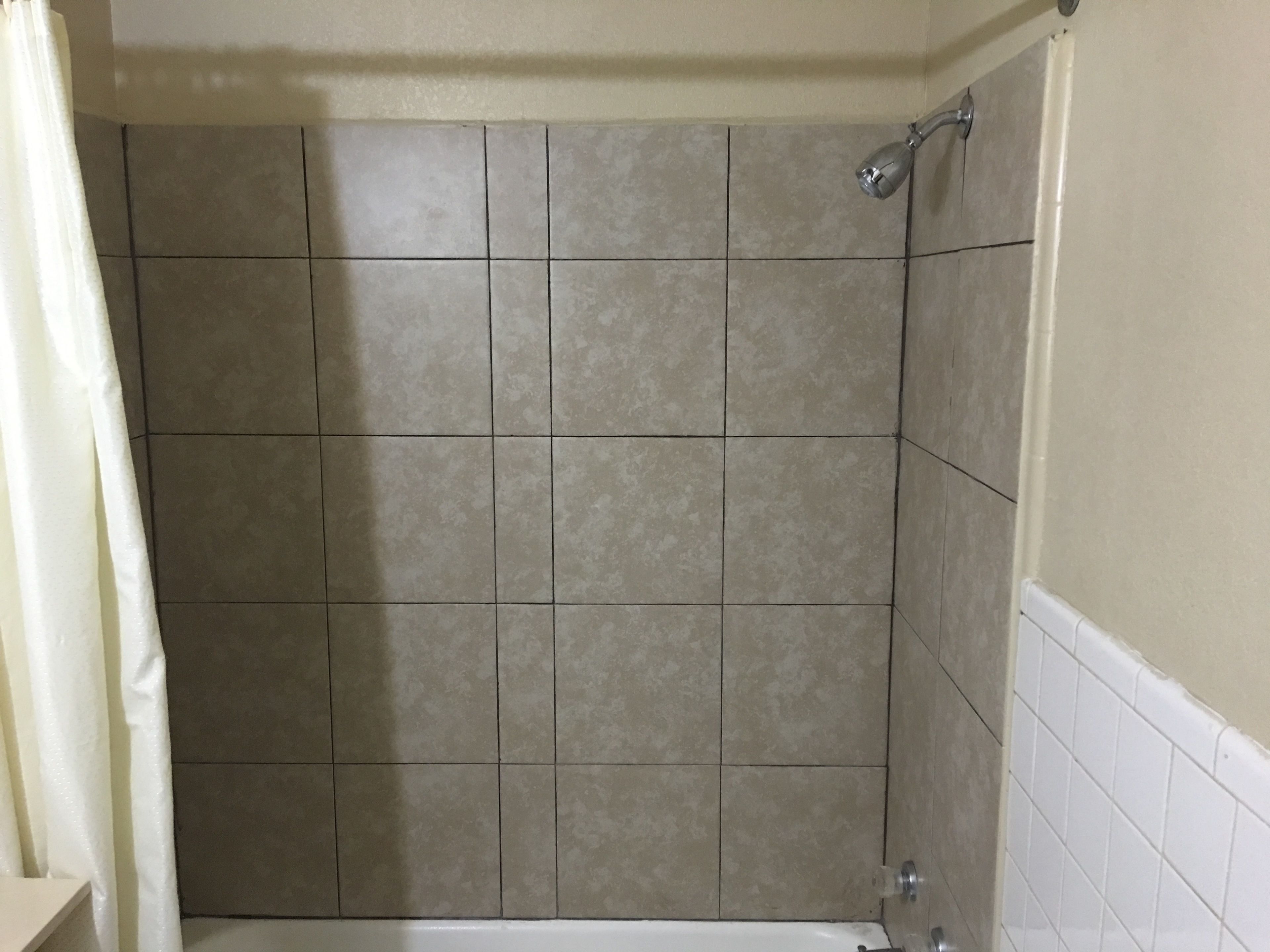 A bathroom with beige tiled walls and a white bathtub.