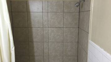 A bathroom with beige tiled walls and a white bathtub.