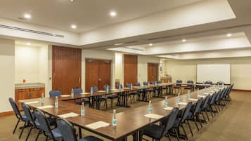 Un salón de conferencias con una larga mesa, sillas, botellas de agua y una pizarra.