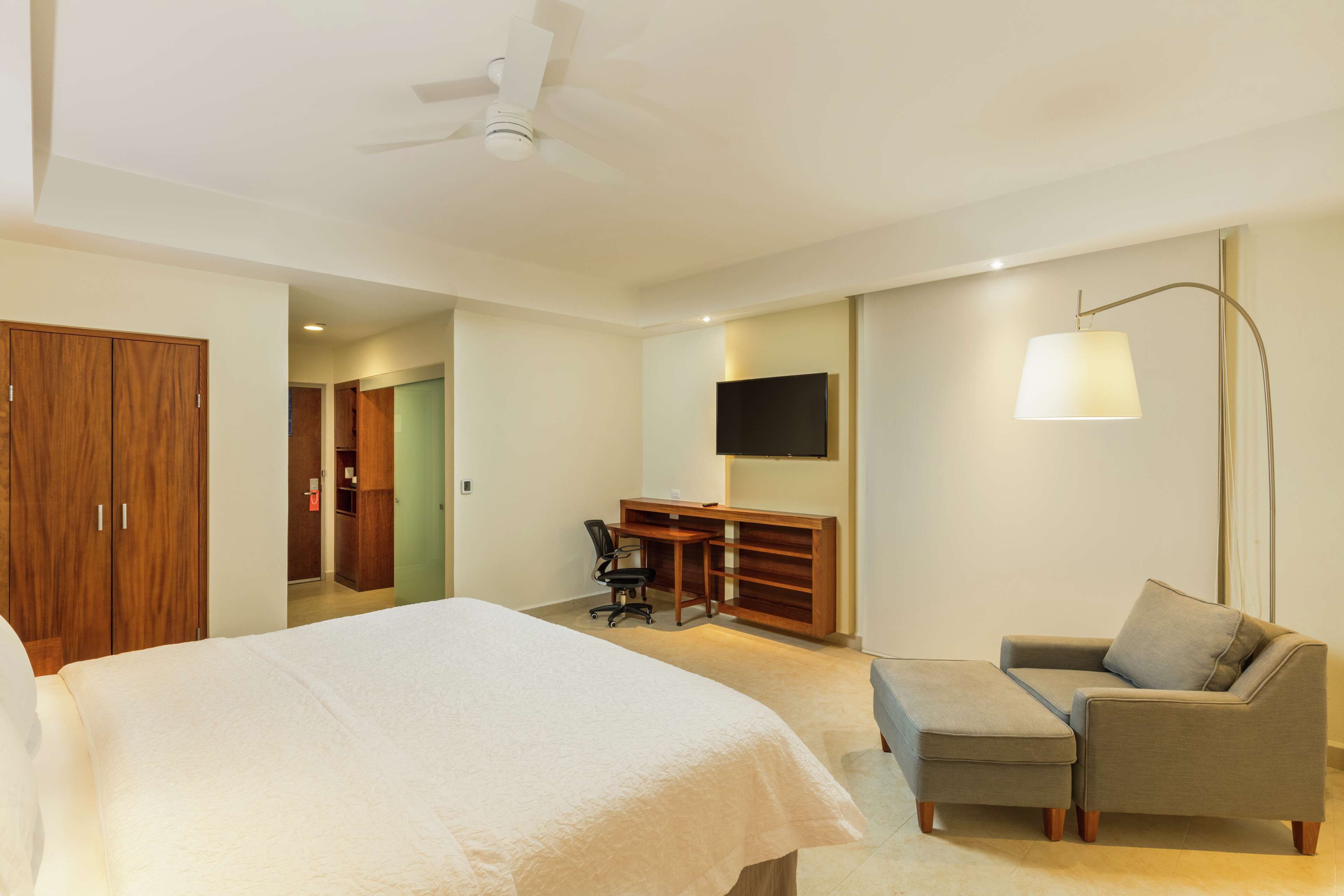 A hotel room with a bed, a desk, a chair, a sofa, a TV, and a ceiling fan.
