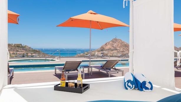 Zona de piscina con sillones de descanso, una sombrilla naranja y una botella de Corona Extra.
