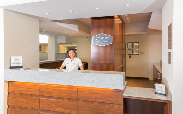 A hotel reception desk with a wooden panel design and a sign for Hampton Inn & Suites by Hilton. - Hampton Inn & Suites by Hilton Los Cabos (San José del Cabo)