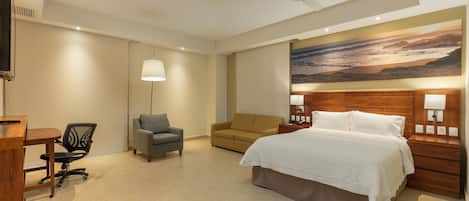 Une chambre d’hôtel équipée d’un lit, d’un bureau, d’une chaise, d’un canapé, d’un ventilateur de plafond et d’un téléviseur fixé au mur.