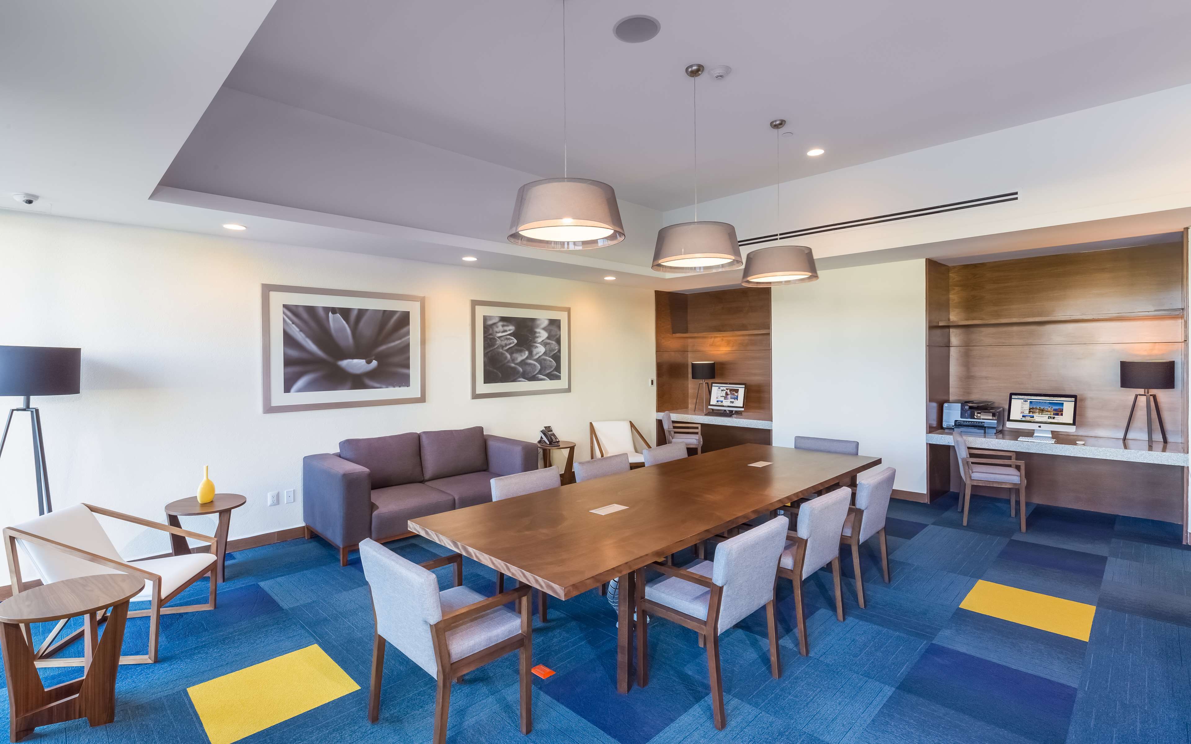 A modern conference room with a wooden table, grey and white chairs, and two pendant lights.