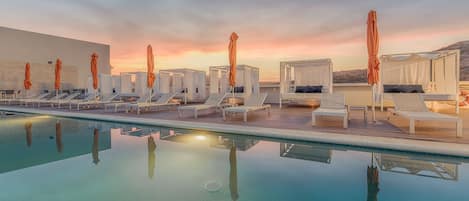 A poolside area with sun loungers and umbrellas, a clear pool, and a sunset view.