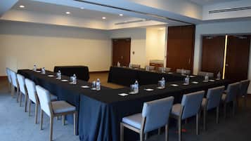Un salón de conferencias con una larga mesa, sillas y botellas de agua.