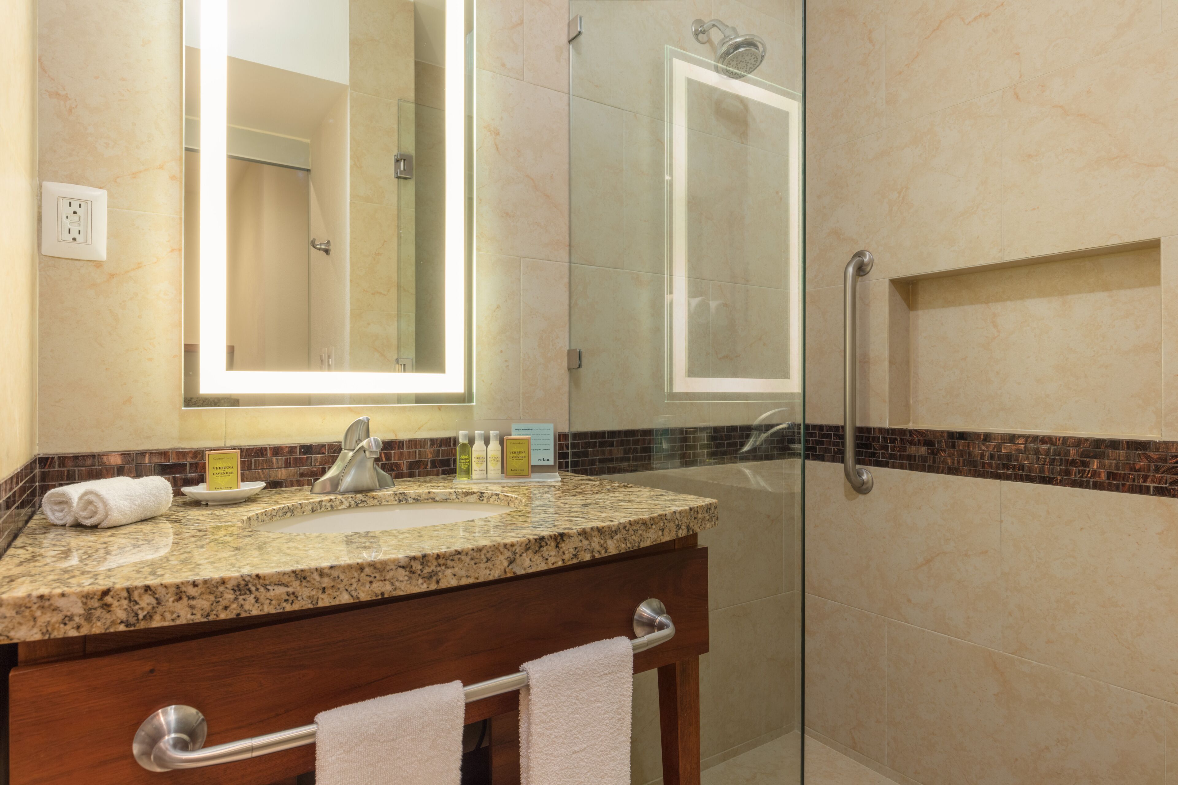 Une salle de bain moderne avec un lavabo surmonté d’un plan de travail en granit, un grand miroir et une douche à parois de verre.