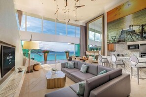 Un moderno salón con sofá, mesa de centro y televisor. Se aprecia una ventana grande con vista al mar.