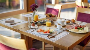 Une table de petit-déjeuner dressée avec des assiettes remplies de nourriture, un vase de fleurs et un verre de jus d’orange.