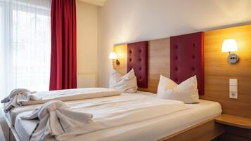 A hotel room with two beds, a wooden headboard, bedside lamps, and a red curtain.
