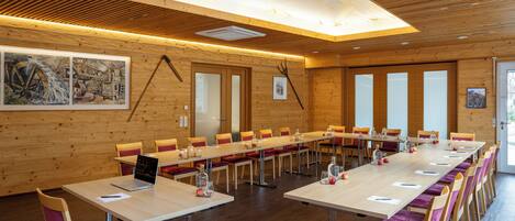 Un salón de conferencias con largas mesas, sillas y techo de madera.