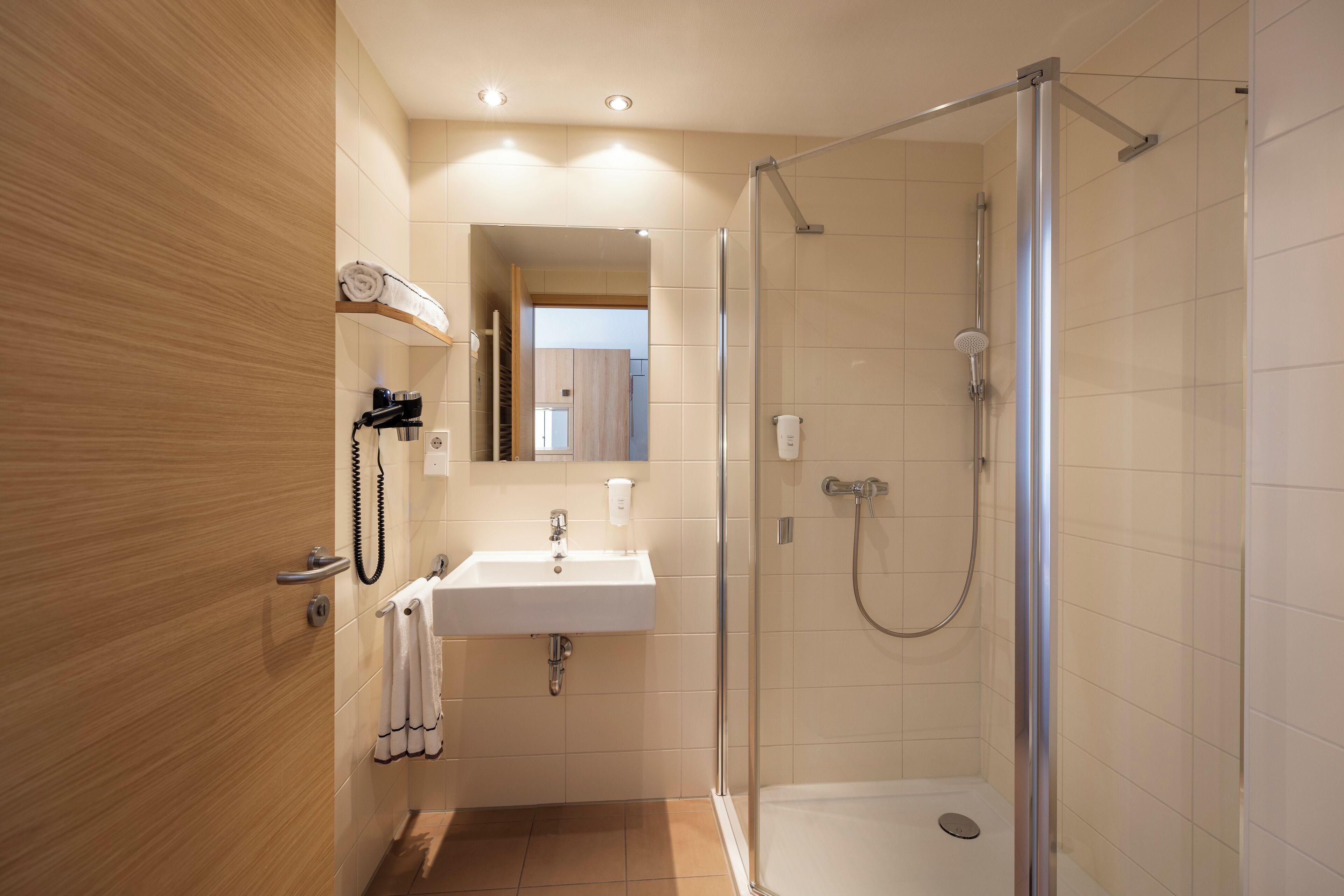 Un baño moderno con ducha de vidrio, lavamanos y perchero para toallas.