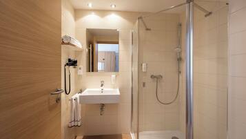 Un baño moderno con ducha de vidrio, lavamanos y perchero para toallas.