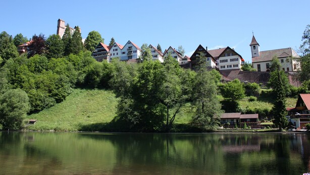 Un village au bord d’un lac, avec des maisons traditionnelles, une église et un clocher imposant.